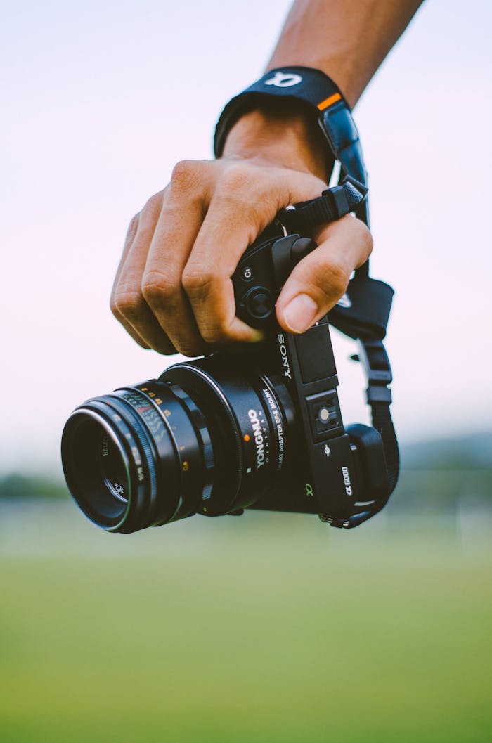 Close-up of a hand holding a vintage camera outdoors with a blurred green background, creating a bokeh effect.
