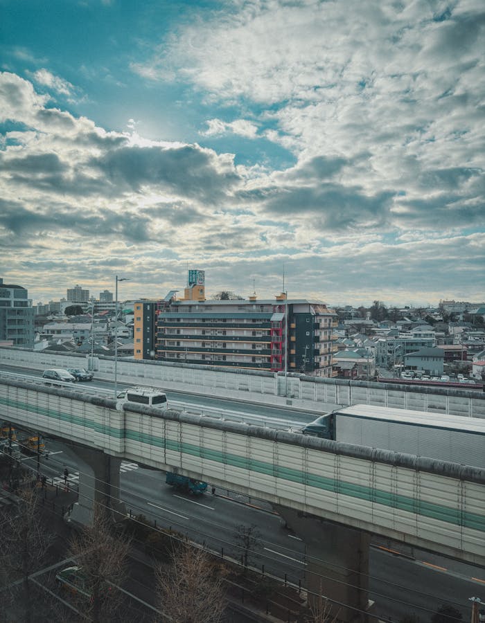 Elevated highway view in Itabashi City, Tokyo, with urban skyline and cloudy sky.
